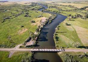 A bridge crosses a winding river in Montana surrounded by lush green grass and trees.