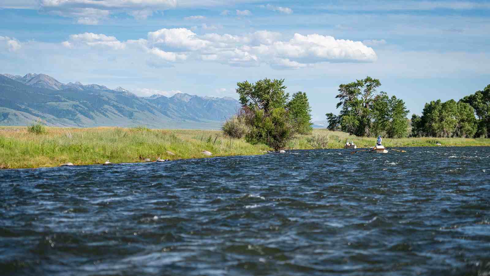A wide view of two boats floating down a Montana river with mountains in the background during a trip with The Tackle Shop.