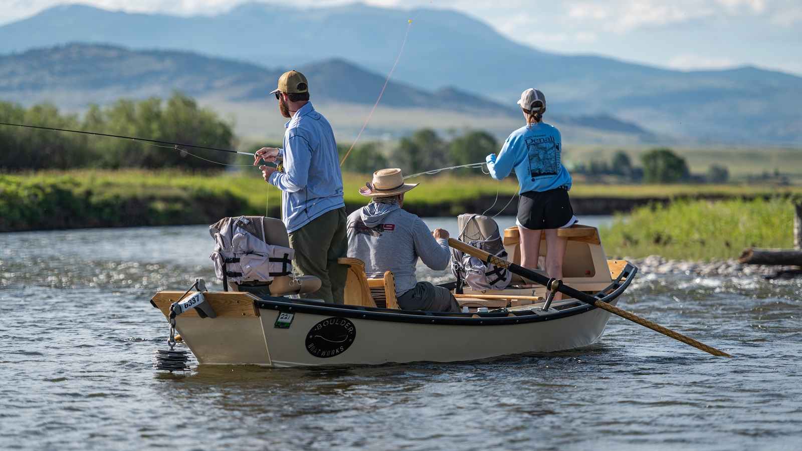 Two people stand in a boat while fly fishing in a Montana river as a guide steers during a trip with The Tackle Shop.