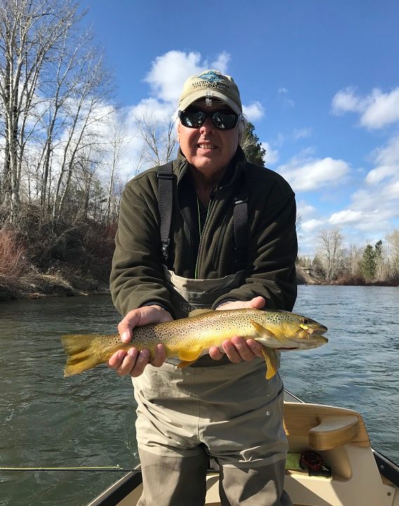 A man holds a fish while standing in a boat floating down a river during a fly fishing trip with The Tackle Shop.