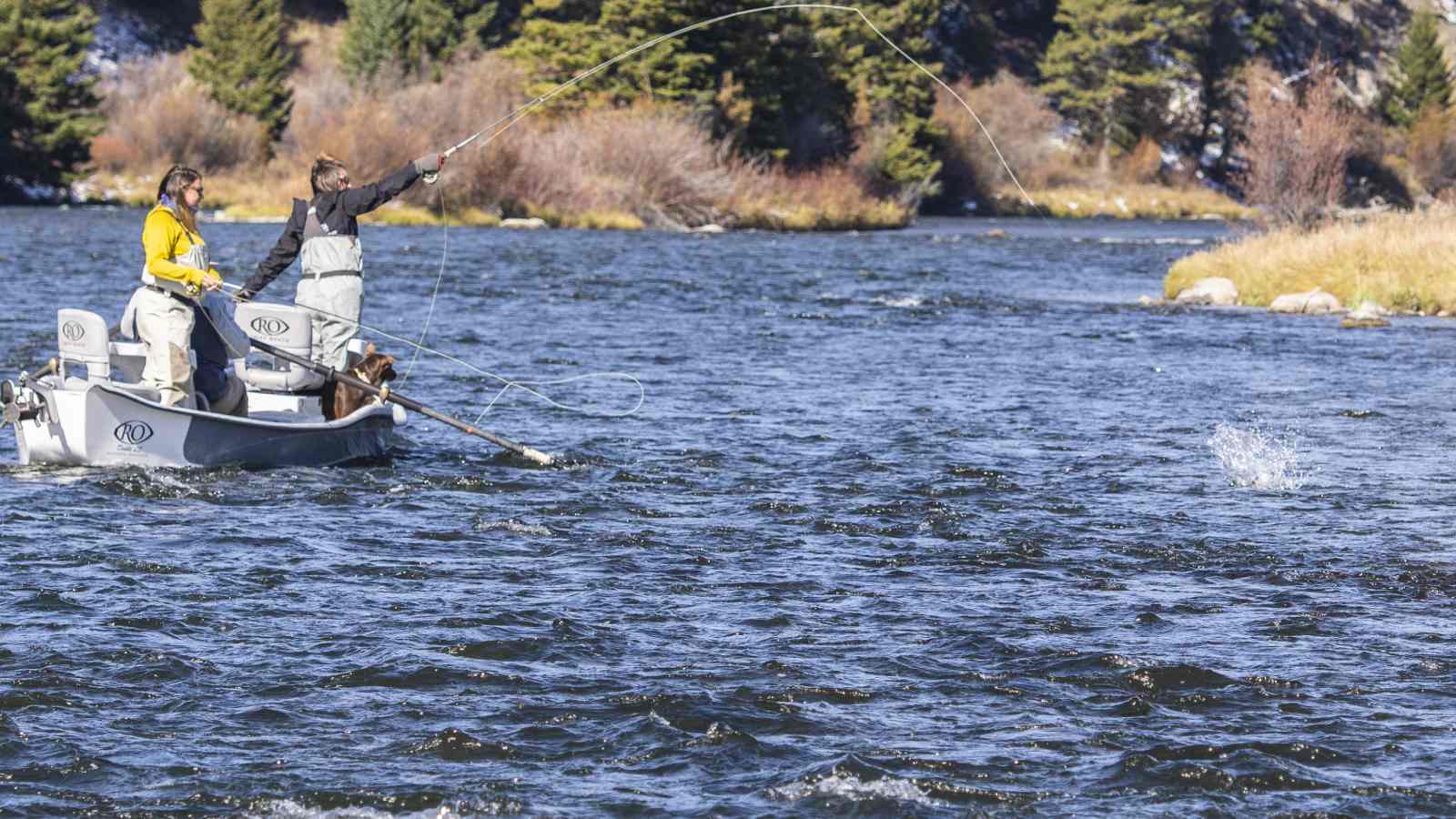 Two women stand in a boat while fly fishing as a guide steers them downriver during a trip with The Tackle Shop.