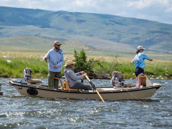 Two people stand in a boat while fly fishing in Montana as a guide steers them downriver during a trip with The Tackle Shop.